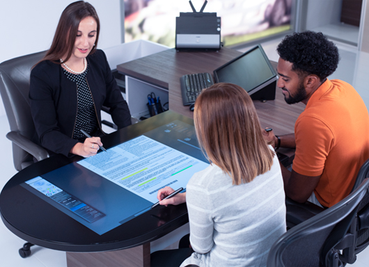 Two customer signing forms on the docuPAD system with an F&I manager.