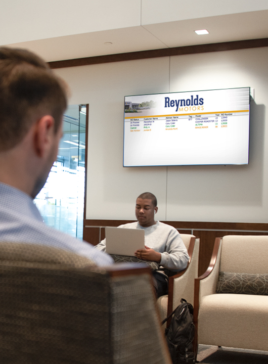 People in a waiting room with the status board showing the status of their vehicle.