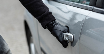 A person dressed in black, with black gloves, implied to be a thief, opening a car door.