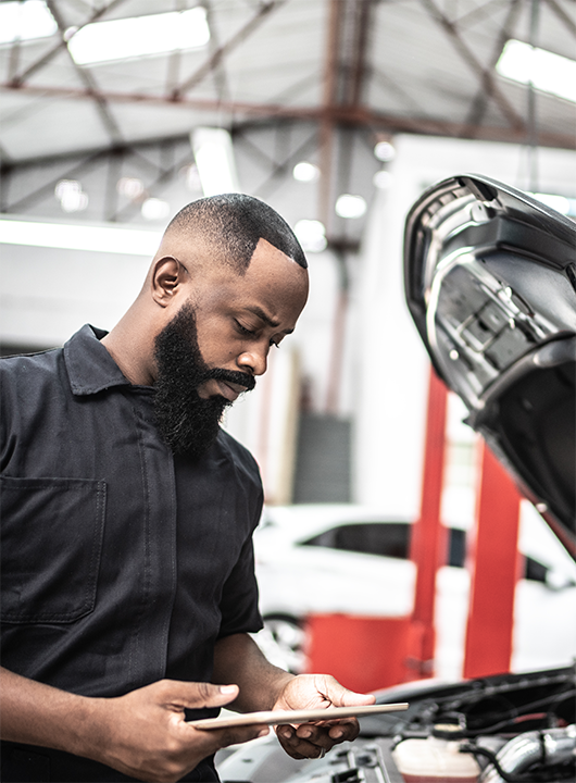 Mechanic on tablet looking at car.