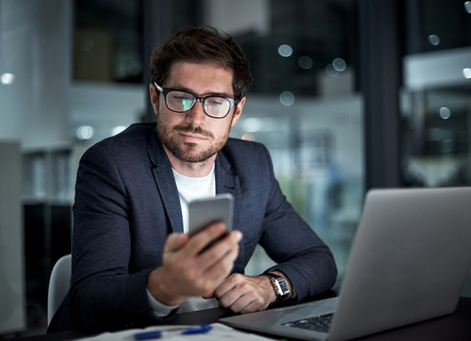 Man sitting at desk, looking at smartphone.