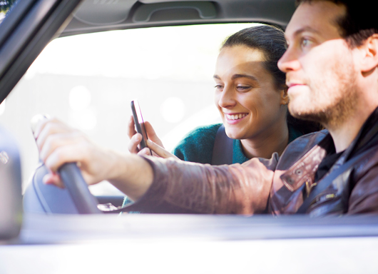 Couple in car, wife looking at phone screen smiling.