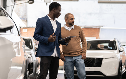Image of two men in car dealership, sales person holding tablet