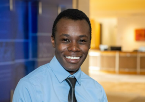 Headshot of Immanuel Sabwami, a smiling African-American male wearing a blue shirt and tie.