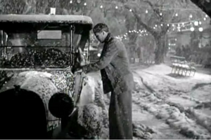 Black and white image of a woman scraping snow off her car.