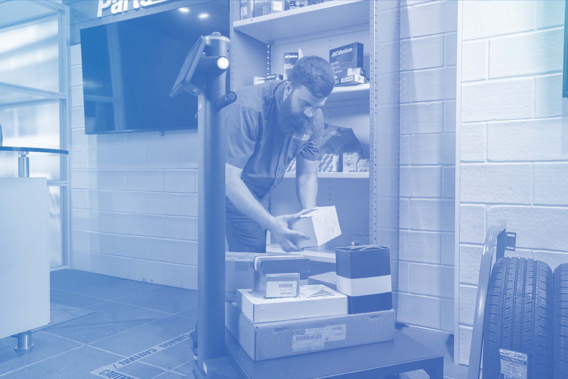 Photo with blue overlay of a Parts department worker loading boxed parts onto Relo, Reynolds' parts-running robot