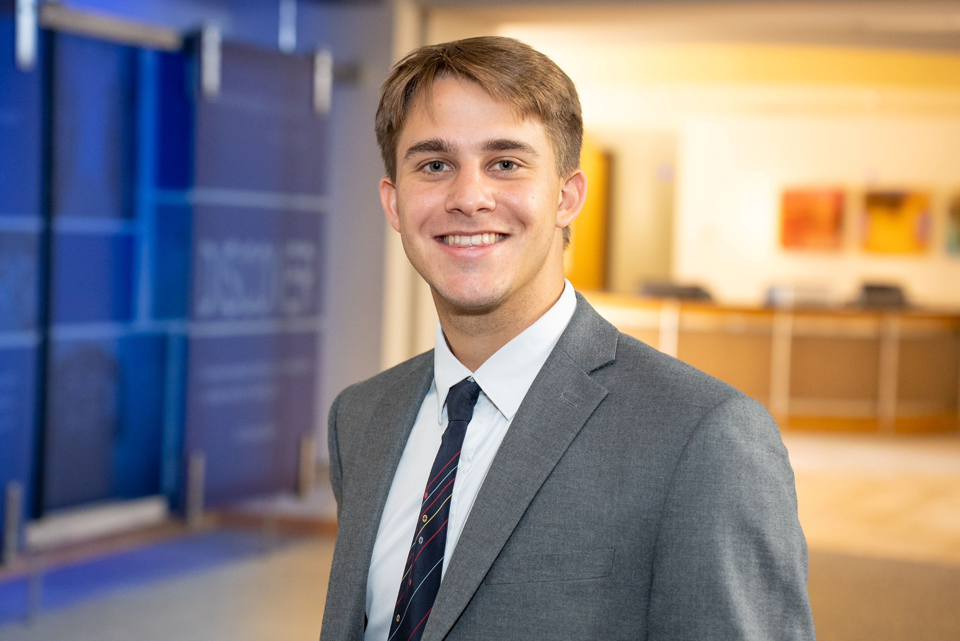 Headshot of a young man with brown hair, in a grey suit with a black tie.