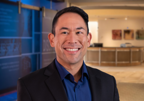 headshot of a man with a blue shirt and black suit